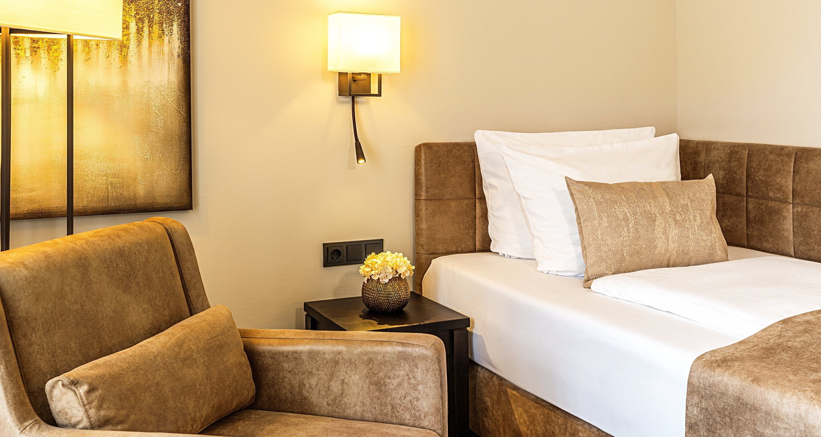 Une chambre d’hôtel avec un lit, une chaise, une table de chevet avec une lampe et un tableau au mur.