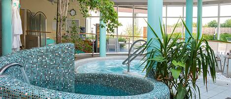 Una piscina interior con mosaicos, una zona de estar y ventanas amplias que dejan entrar luz natural.