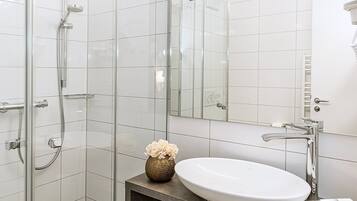 Un baño moderno con cabina de ducha de vidrio, un lavabo blanco y un espejo.