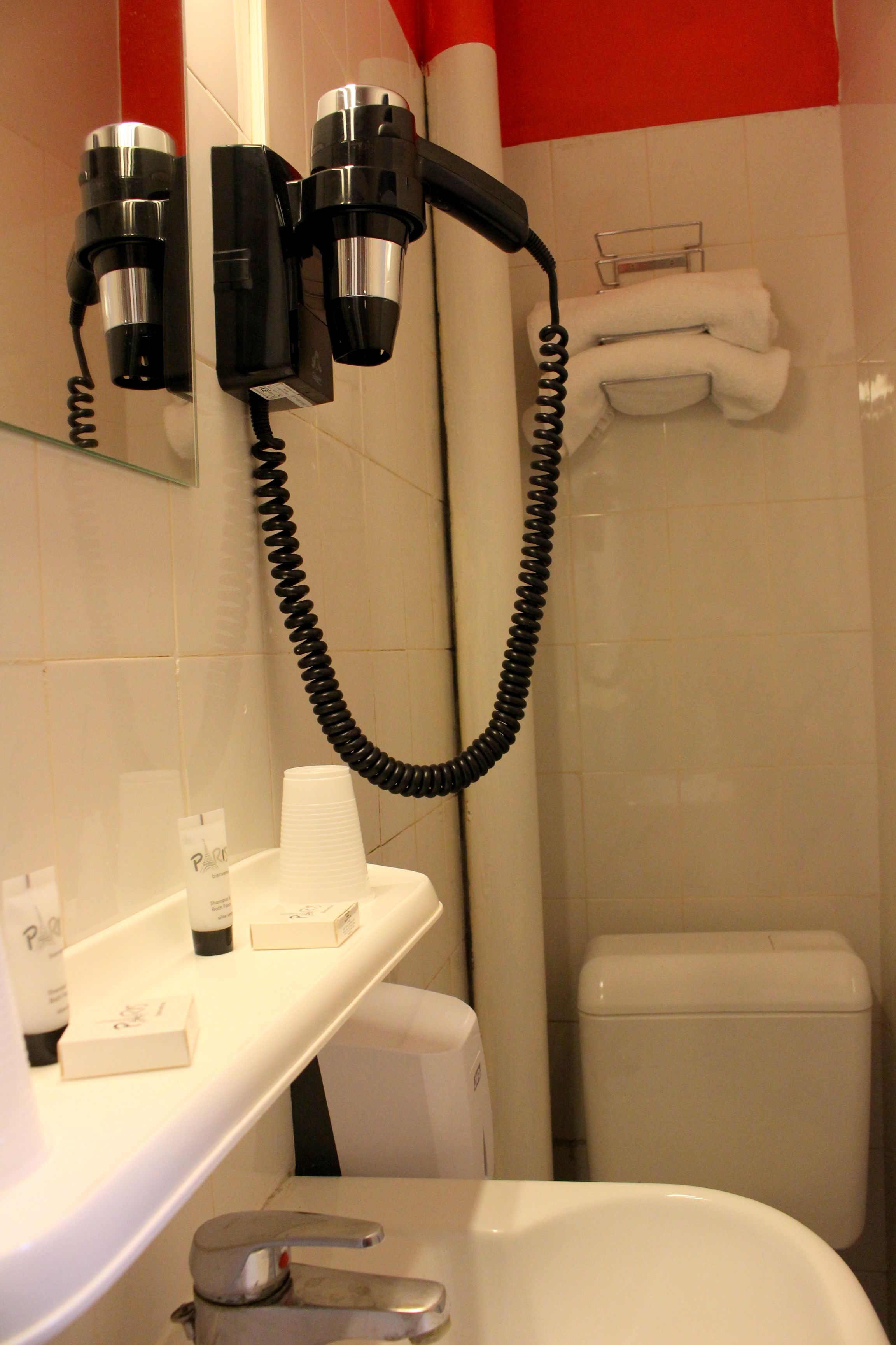 A bathroom with a hairdryer mounted on the wall, a towel rack, and a toilet.