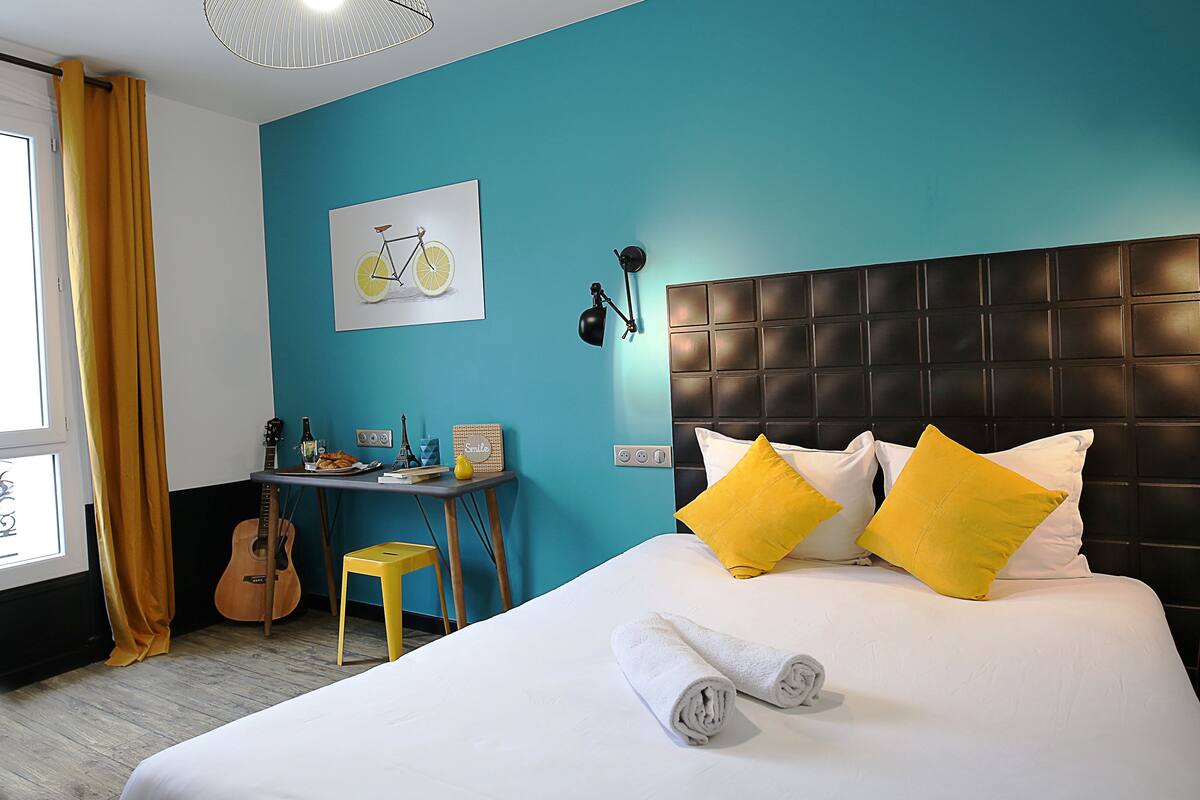 Ein Hotelzimmer mit Bett, Schreibtisch, einer Gitarre und einem Wandbild mit einem Fahrrad.