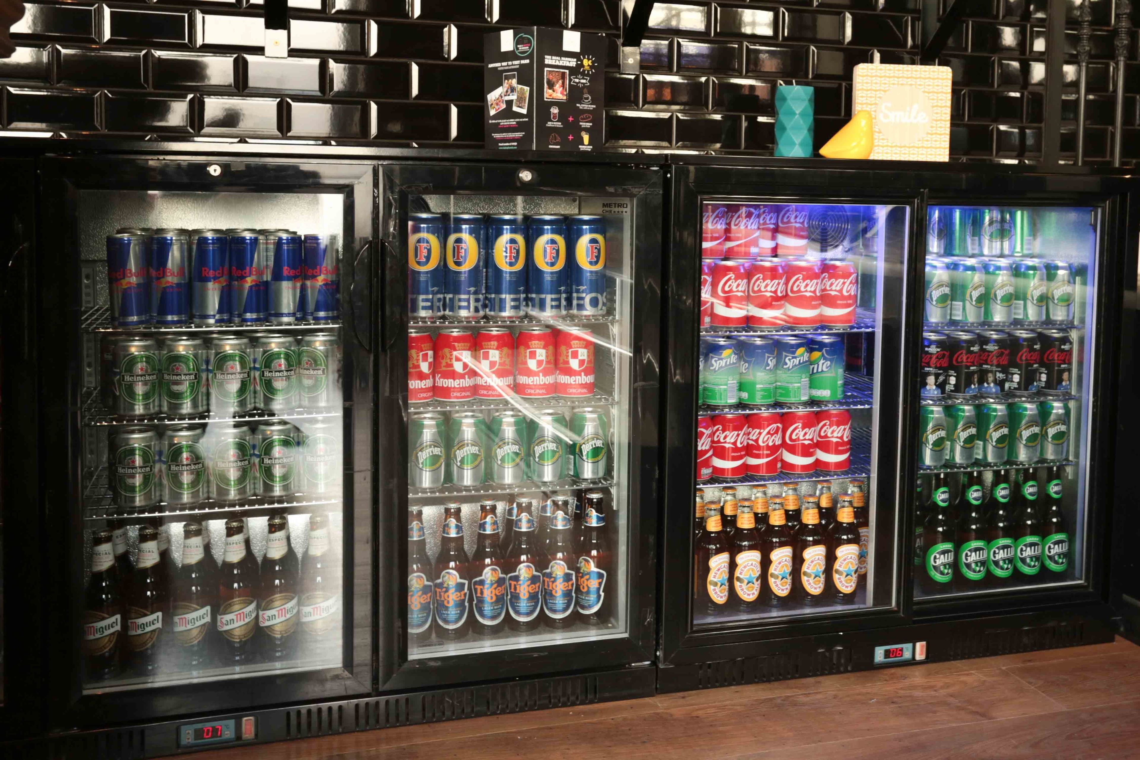 A row of beverage vending machines with various brands like Heineken, Red Bull, Coca-Cola, Sprite, and San Miguel.