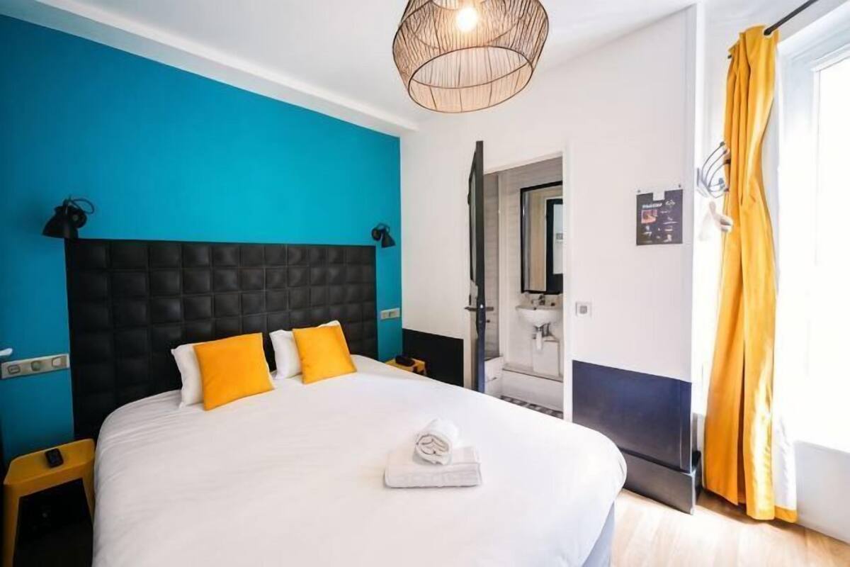 Ein Schlafzimmer mit einem großen Bett, einem Kopfteil, einem Nachttisch, einer stehenden Lampe und einer Badezimmertür.