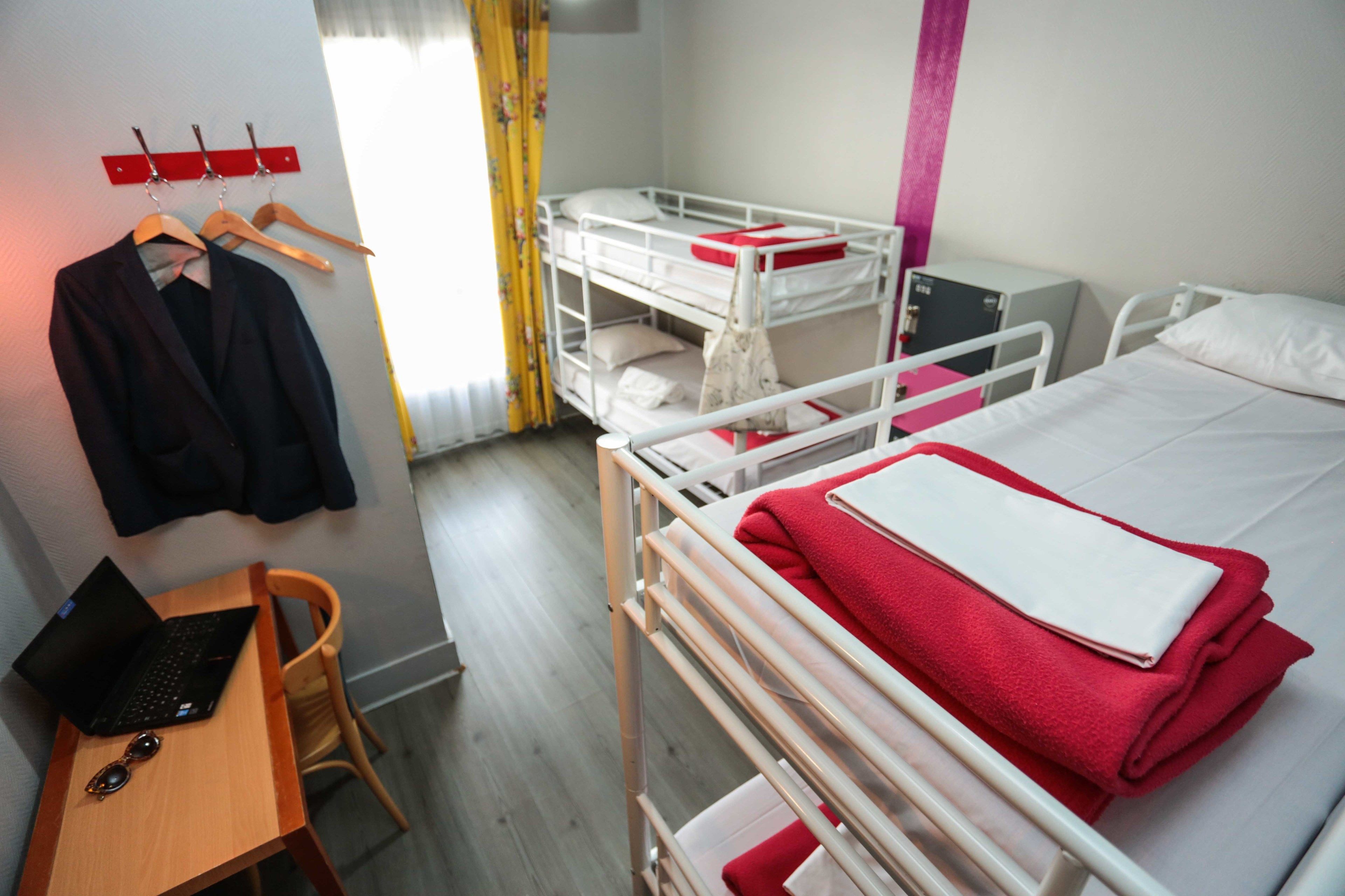 Et hotelværelse med køjesenge, et skrivebord med en bærbar computer og en stol.