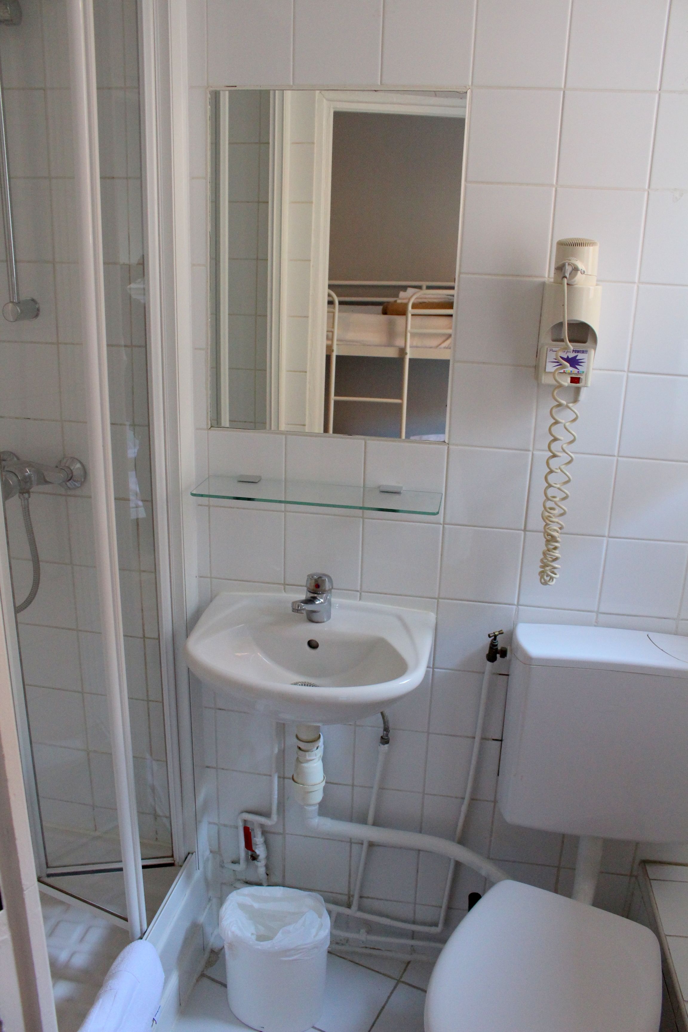 Un baño con estante de vidrio, lavamanos blanco, inodoro y cabina de ducha.