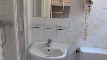 A bathroom with a glass shelf, a white sink, a toilet, and a shower enclosure.