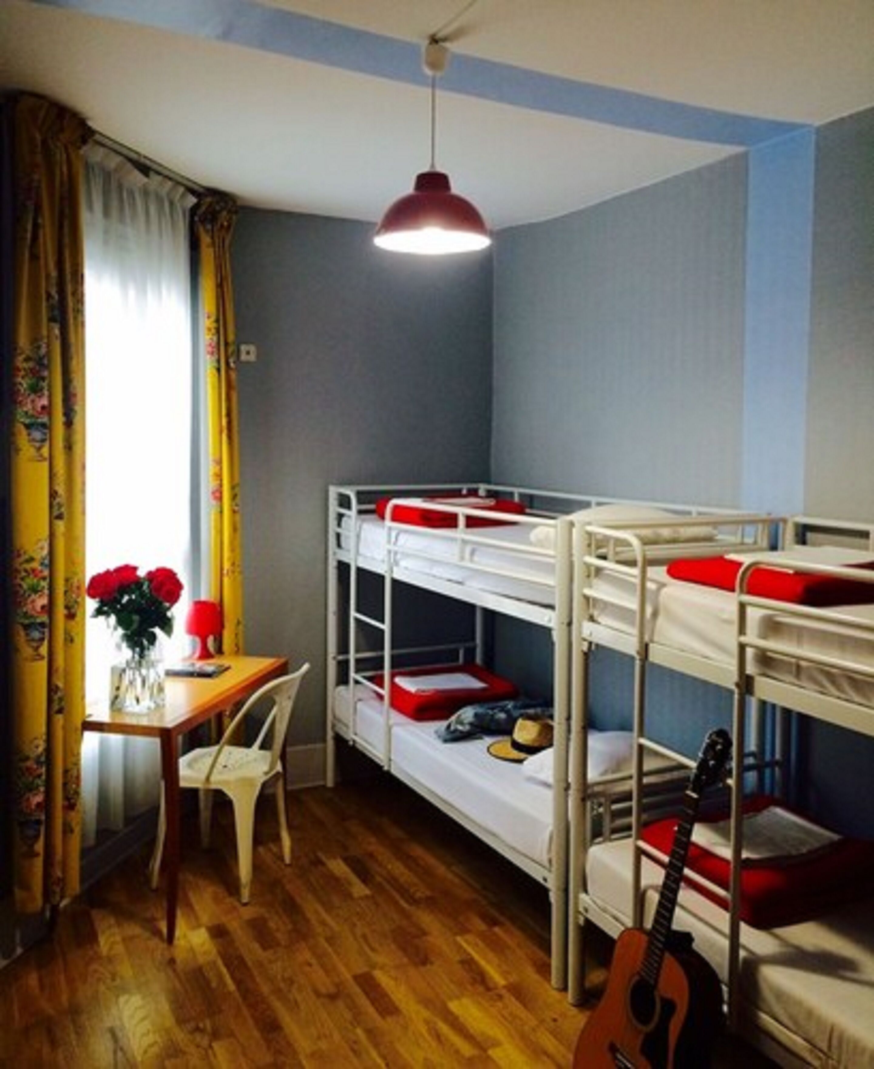 Ein Schlafsaalzimmer mit Etagenbetten, einem Schreibtisch, einem Stuhl, einer Gitarre und einer Pendelleuchte.