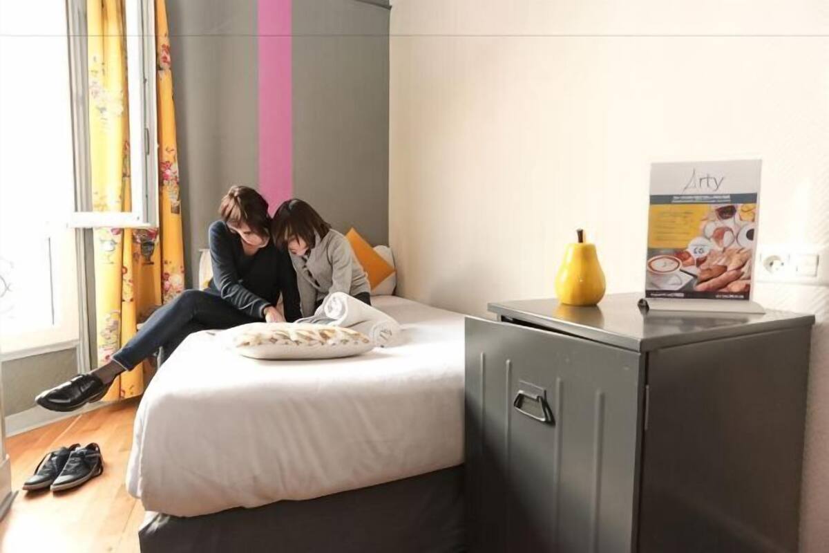 Ein Zimmer mit einem Bett, einem kleinen Schrank und einem Fenster mit Vorhängen.