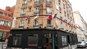 A corner building with multiple flags, a black storefront, and a bicycle parked in front. - Arty Paris Porte de Versailles by River - Hostel (Paris)