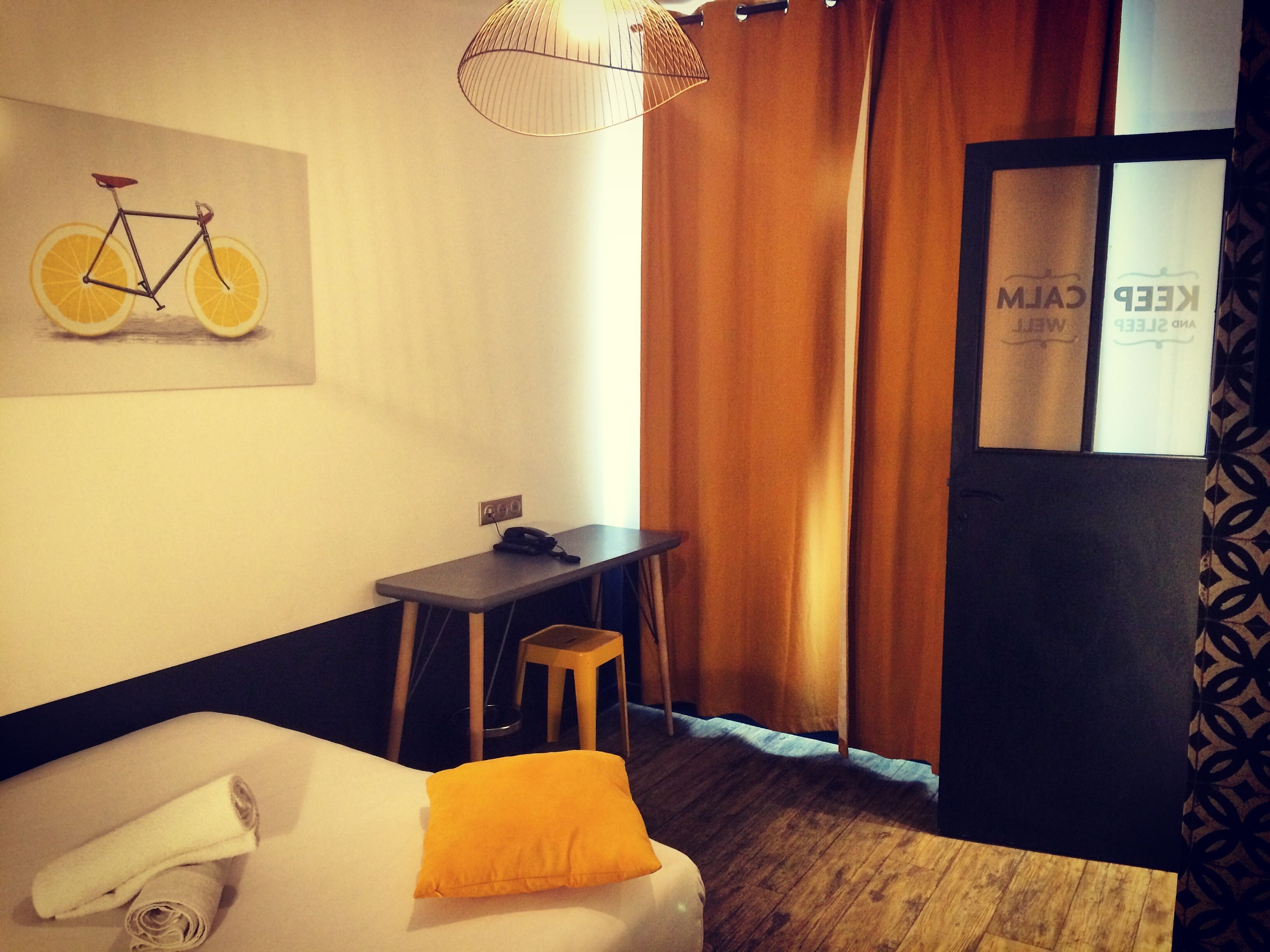 Une chambre d’hôtel avec un lit, un bureau, une chaise, une lampe et une fenêtre avec des rideaux.