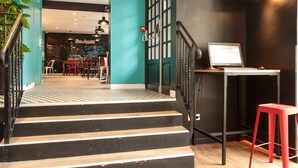 A staircase leading to a bar area with a laptop on a table, a red stool, and a plant. - Arty Paris Porte de Versailles by River - Hostel (Paris)