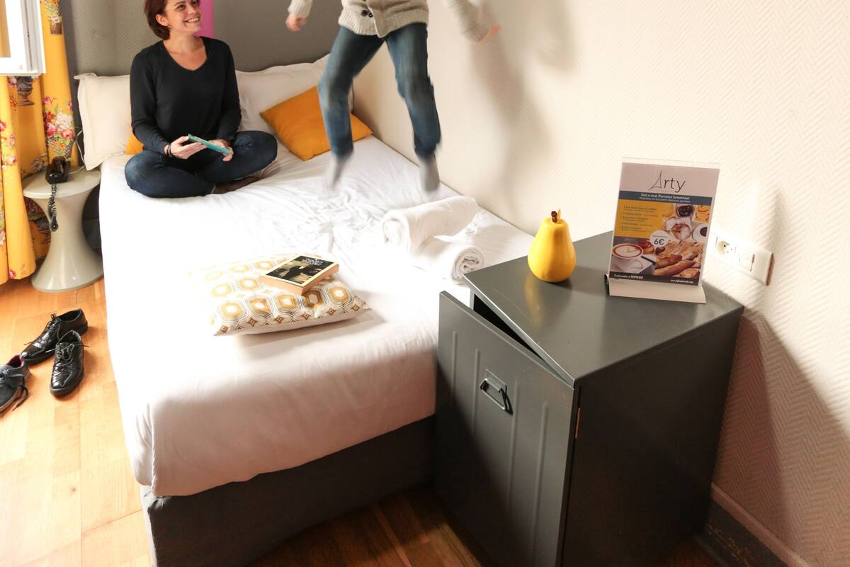Ein Schlafzimmer mit einem Bett, einem Nachttisch, einer kleinen Kommode und einem Fenster mit Vorhängen.