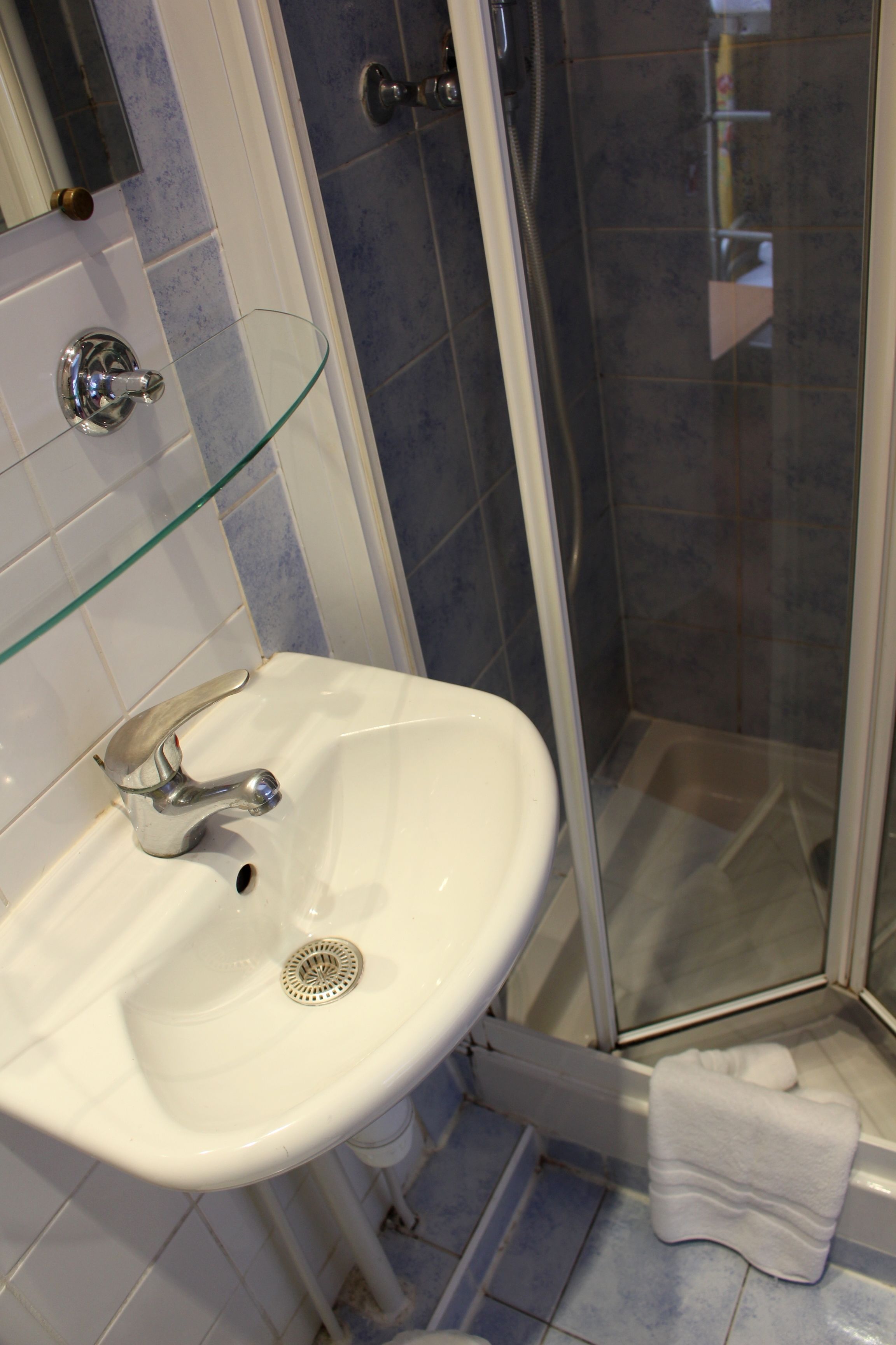 A bathroom with a glass shower enclosure, a white sink with a chrome faucet, and a towel on the floor.