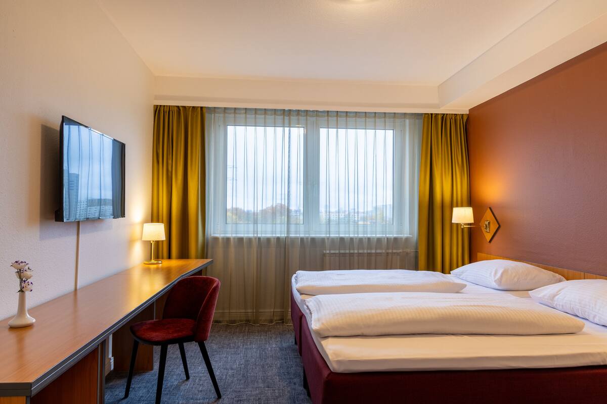 Een hotelkamer met een bed, een bureau, een stoel, een televisie en een raam met gordijnen.