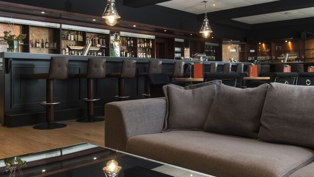 A bar area with multiple stools, a sofa, and a bar counter with various bottles and glasses.
