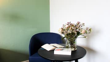 Una mesa redonda con una silla azul, un jarrón de flores y un libro abierto.