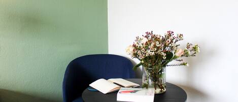 Una mesa redonda con una silla azul, un jarrón de flores y un libro abierto.
