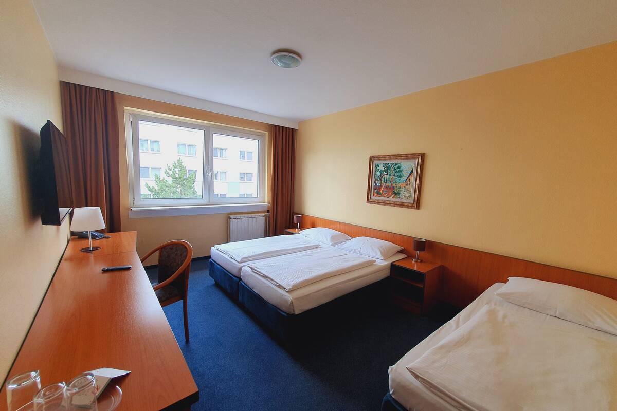 Hotelkamer met een bed, bureau, stoel, raam met gordijnen, schilderij aan de muur en een radiator.