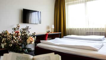 Una habitación de hotel con dos camas, un escritorio, un televisor y una ventana con cortinas.