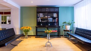 A modern lobby with a black leather sofa, a glass table with a vase of flowers, and a bookshelf against a teal wall.