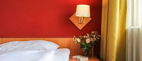 A hotel room with a bed, a nightstand with a lamp, and a vase with flowers.