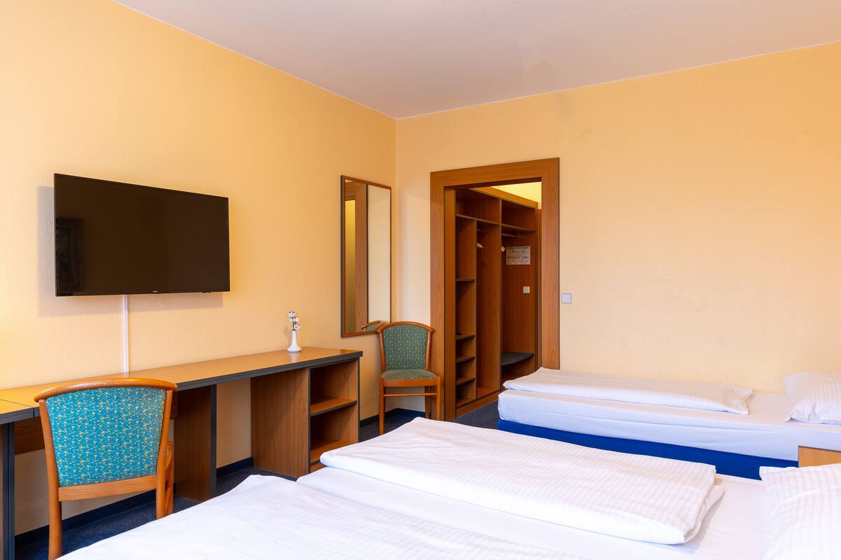 Een hotelkamer met een bureau, stoel, twee bedden, een televisie en een kledingkast.