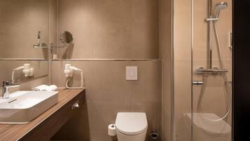 A modern bathroom with a double sink vanity, a toilet, a shower enclosure, and a mirror.