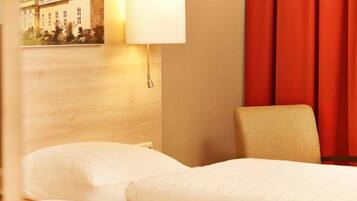 Une chambre d’hôtel avec un lit, une chaise, une lampe et un tableau accroché au mur.