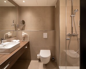 A modern bathroom with a wooden vanity, a toilet, a shower enclosure, and a large mirror.