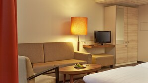 Habitación de hotel con sofá, una mesita con frutero, televisor sobre una estantería de madera y un armario.