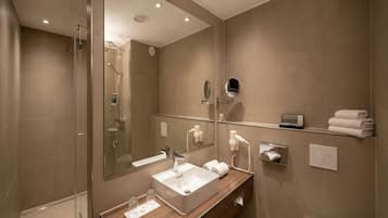 A modern bathroom with a glass shower enclosure, a wooden vanity, a large mirror, and a toilet.