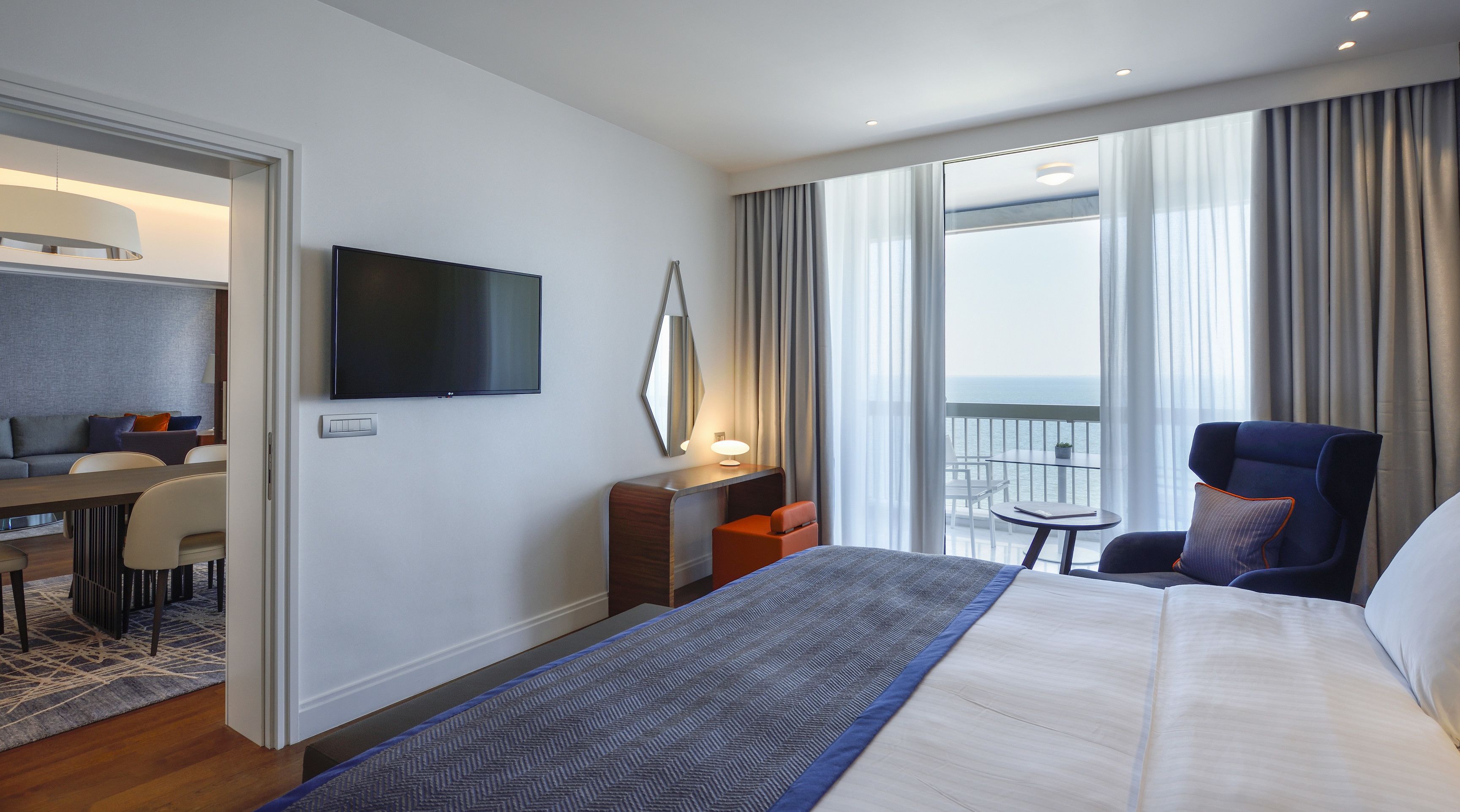 Une chambre d’hôtel équipée d’un lit, d’un bureau, d’une chaise, d’une télévision et d’un balcon avec vue sur la mer.