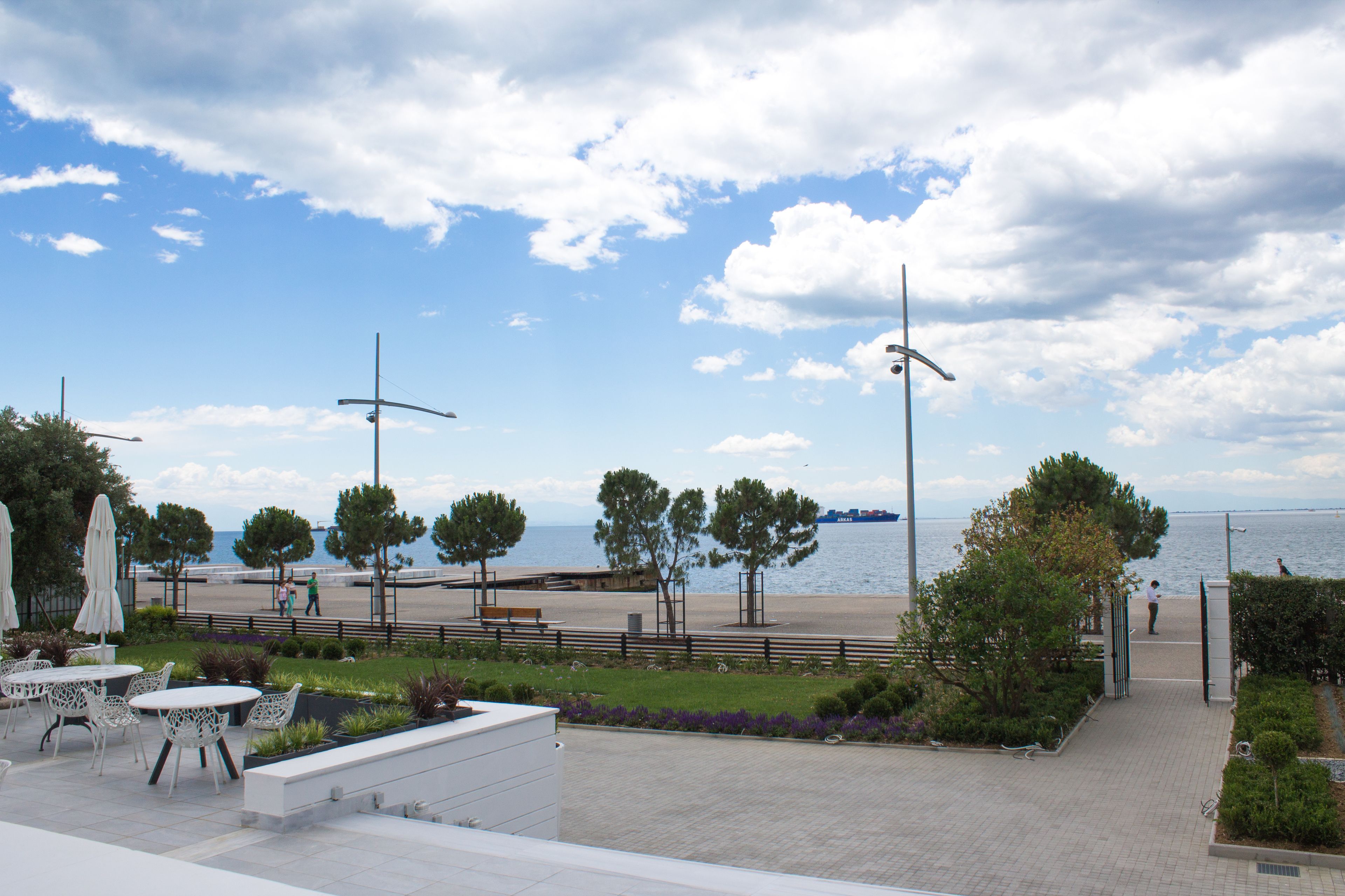 A waterfront promenade with outdoor seating, trees, and a view of the sea.