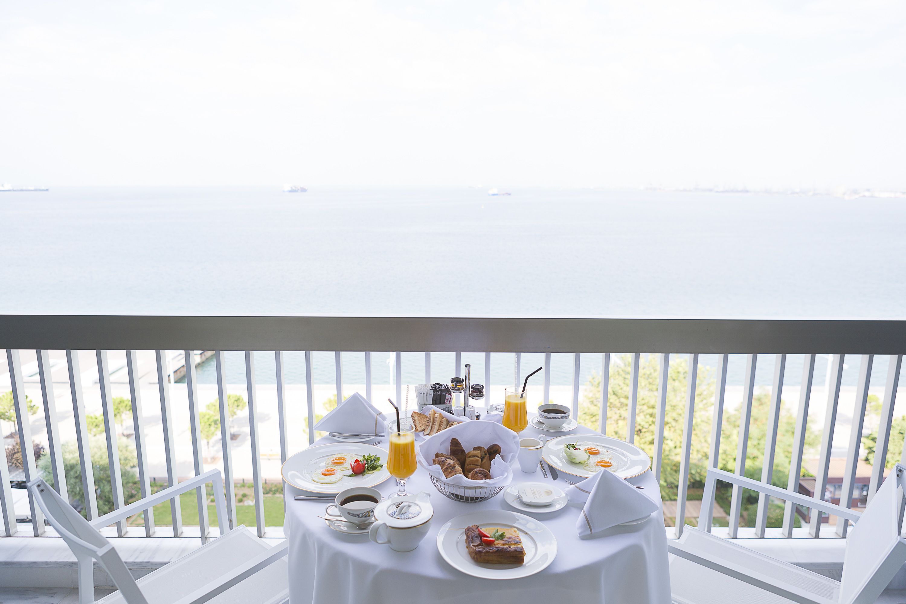 A balcony with a table set for breakfast, overlooking a body of water.
