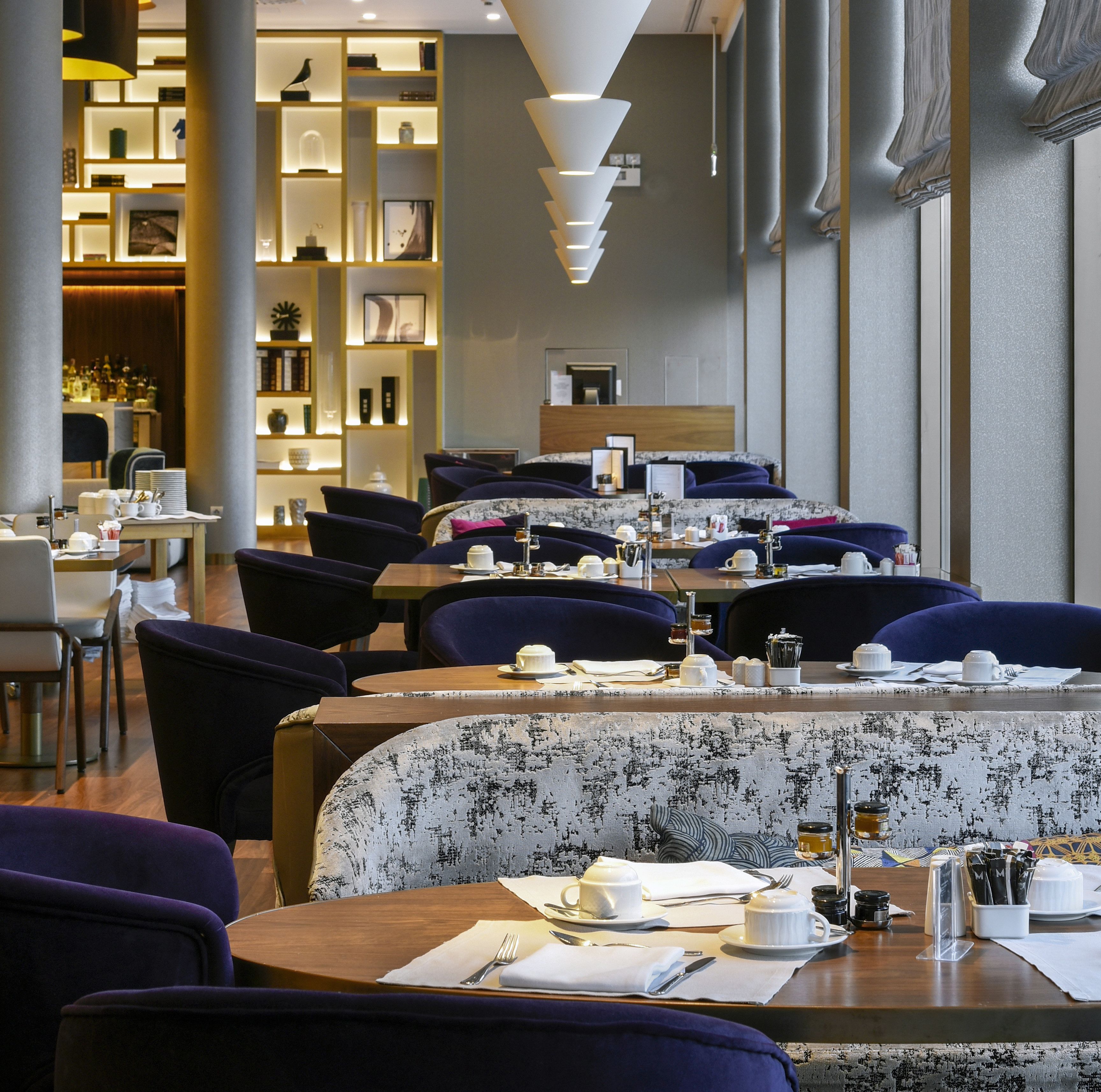A restaurant with multiple tables, dark blue upholstered chairs, and a patterned tablecloth.