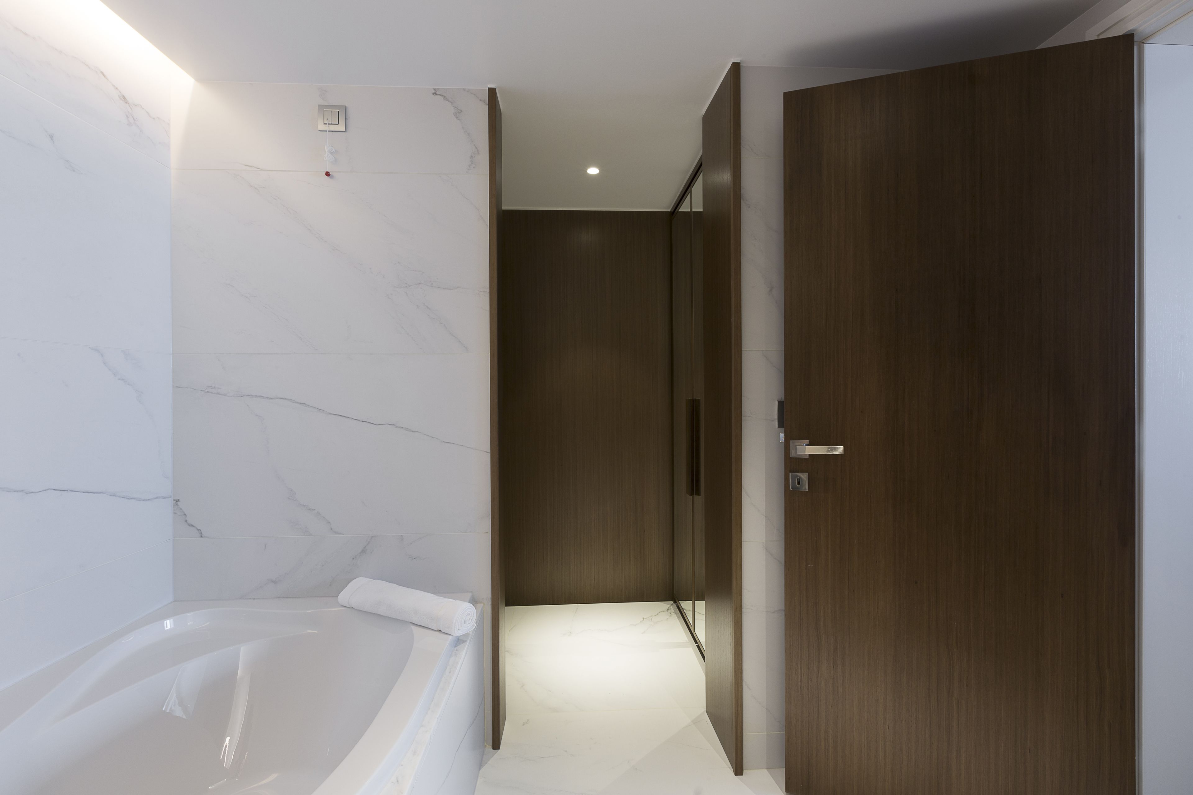 Un baño moderno con pared de mármol, puerta de madera y bañera.