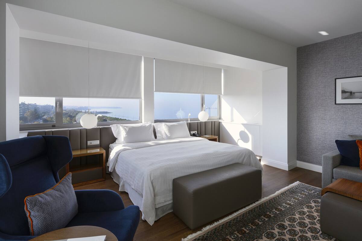 A modern hotel room with a large bed, seating area, and a view of the city.