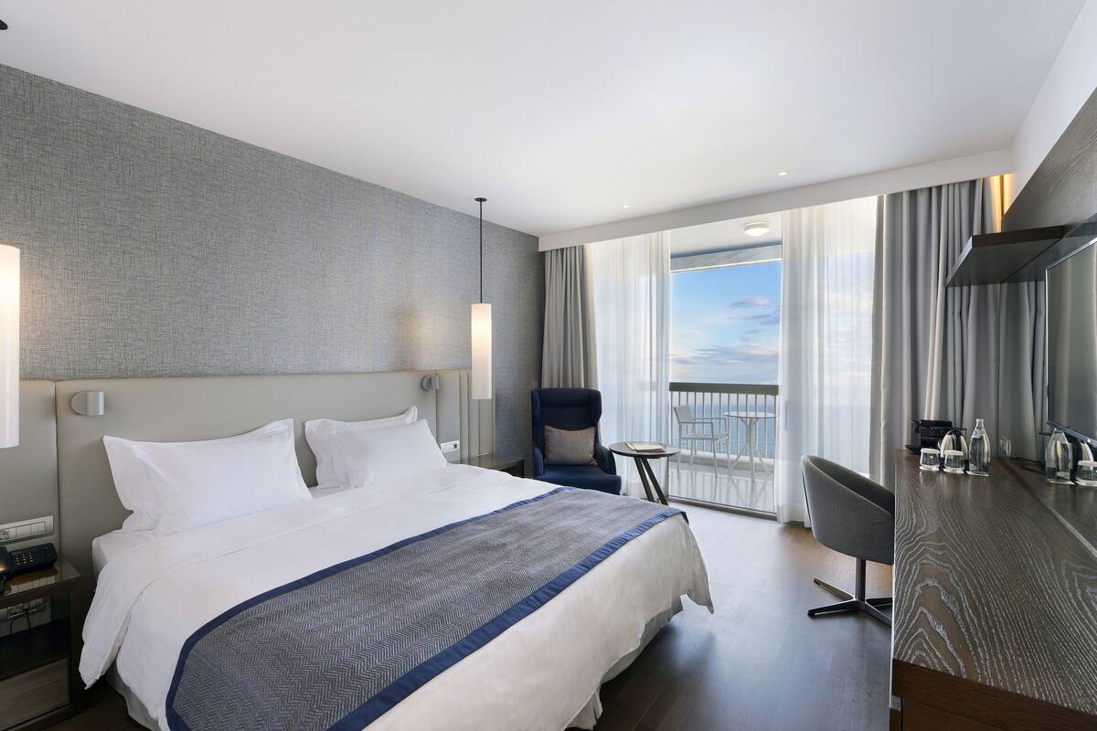 A modern hotel room with a large bed, a seating area with a view, and a minibar.