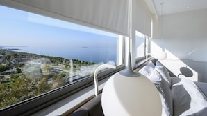 Moderni hotellihuone, jossa on suuri ikkuna, josta avautuu näkymä rannikkoalueelle, mukaan lukien tie ja viheralueet.