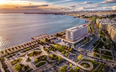 An aerial view of a coastal city with a prominent hotel featuring a modern design, a marina, and a well-planned urban layout with roads and greenery.