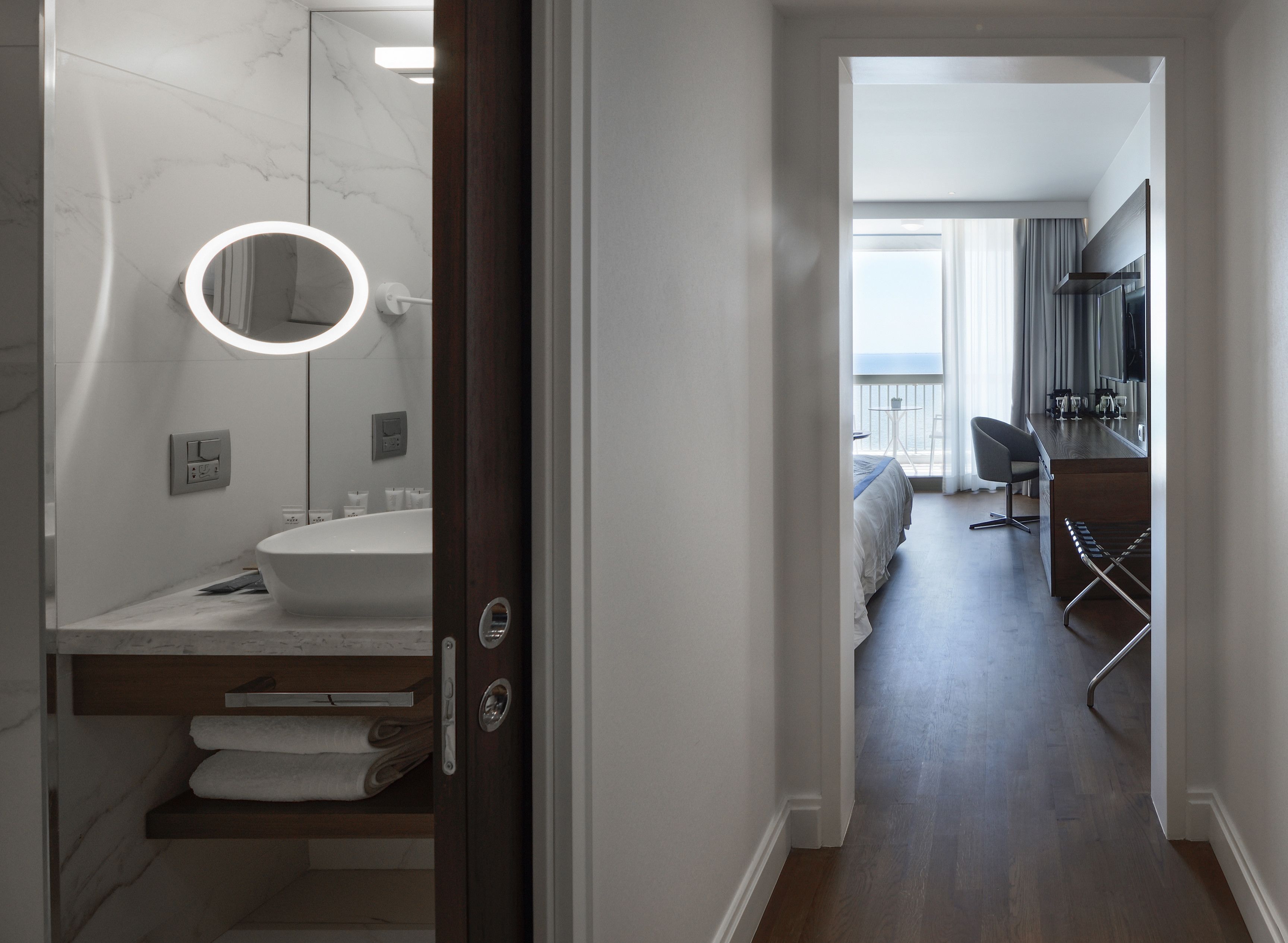 A modern bathroom with a marble vanity, a round mirror, and a built-in toilet.