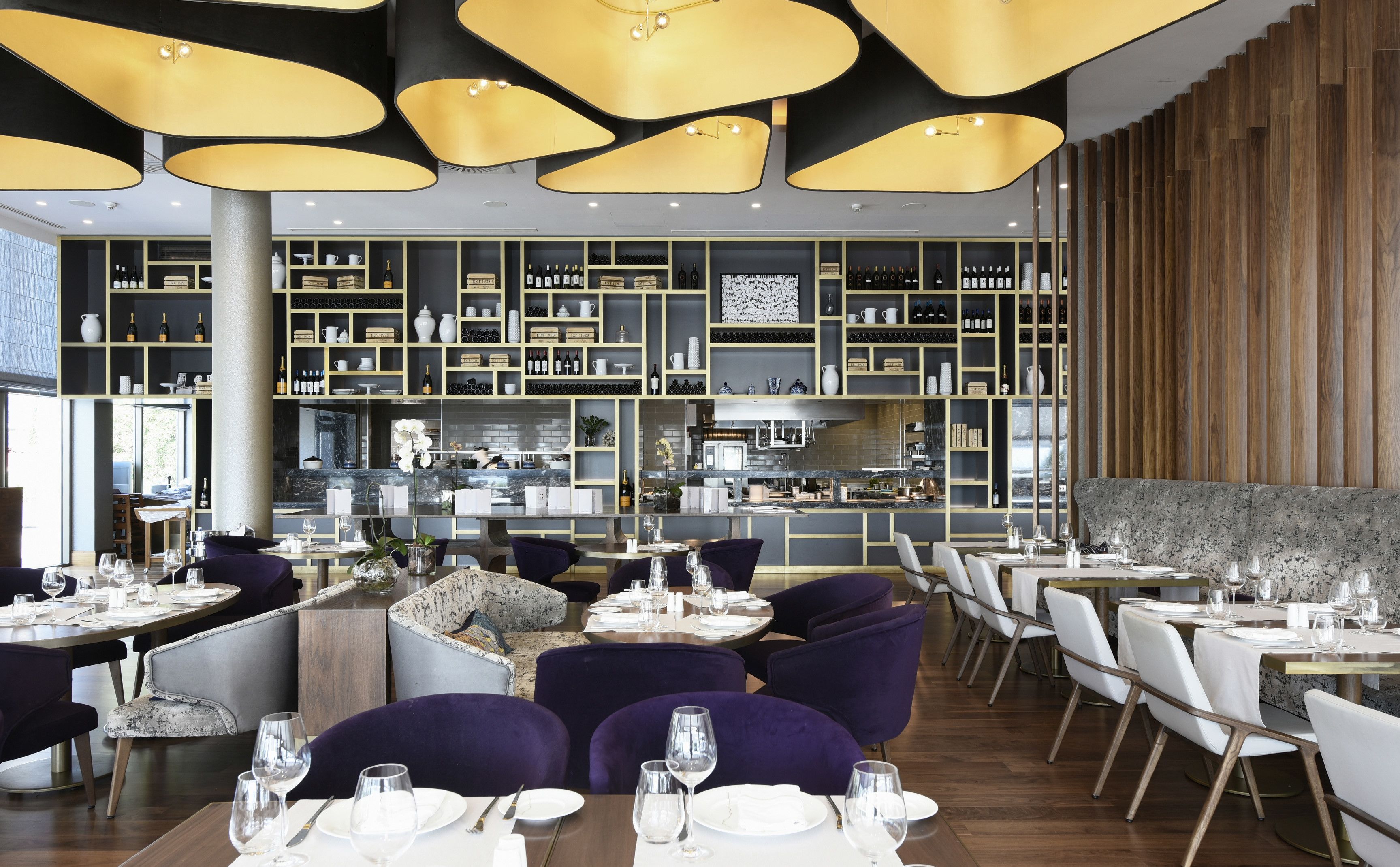Un interior de restaurante moderno con mesas redondas, sillas moradas y una bodega de vino al fondo.