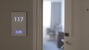 Puerta de una habitación de hotel con un panel digital que muestra el número de habitación 117 y un panel interactivo que indica 'Por favor, toque'.