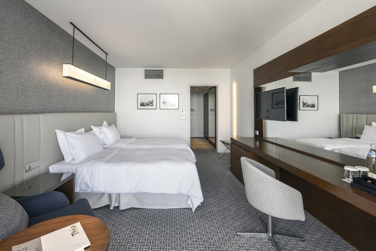 A hotel room with a large bed, a desk with a mirror, a chair, and a TV.