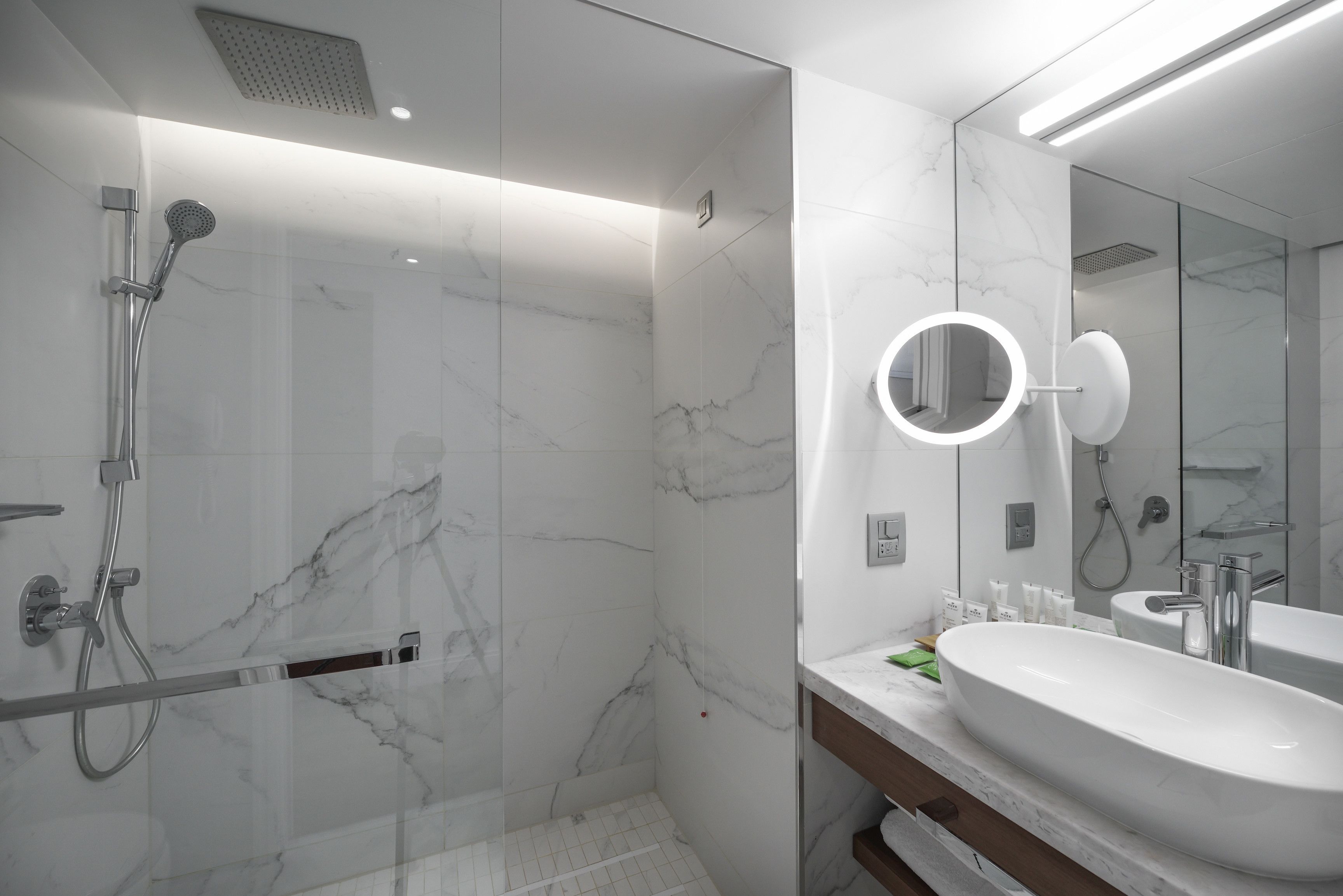 A modern bathroom with a large mirror, a sink, and a shower area with a glass door.