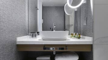 Un baño moderno con un lavamanos blanco grande, un espejo con luz circular y un perchero para toallas.
