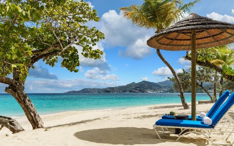 A beach with a lounge chair and a thatched umbrella.