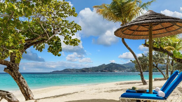 Een strand met een strandstoel en een rieten parasol.