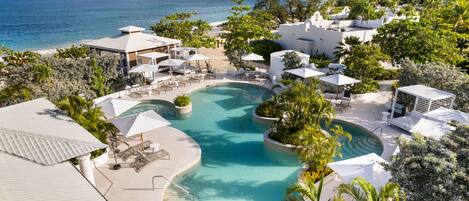 A resort with a pool, lounge chairs, umbrellas, and a view of the sea and mountains.