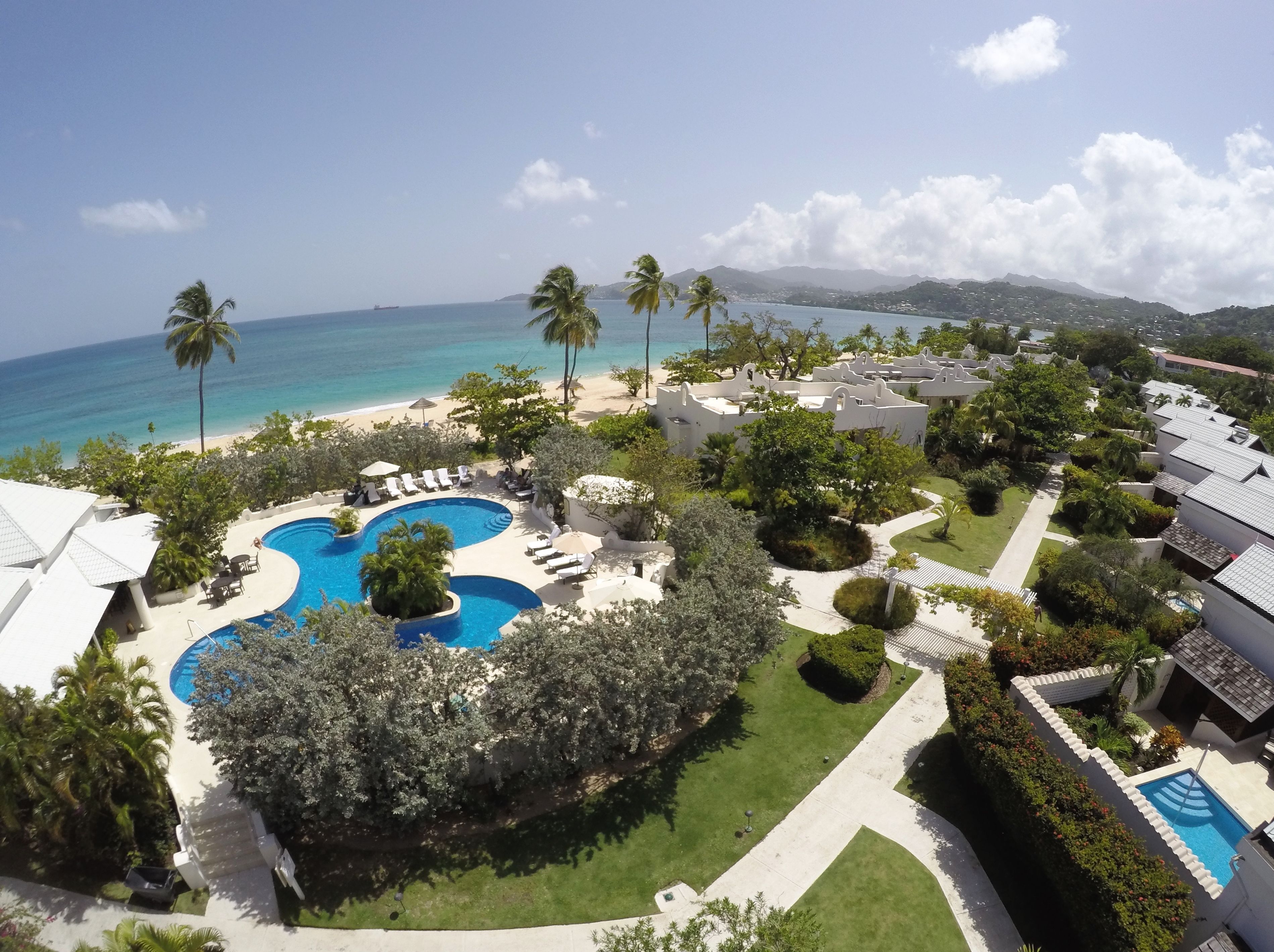 A resort with a large swimming pool, palm trees, and a view of the ocean.